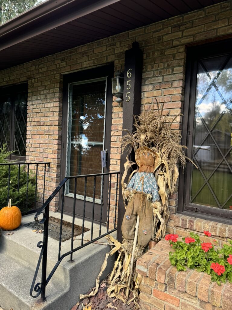Brick front porch with scarecrow and pumpkin decor