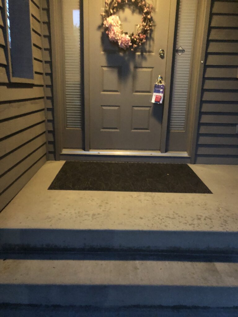 Front entrance with gray door, floral wreath, and concrete steps.